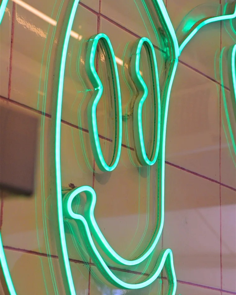 Letreiro de neon verde com a carinha sorridente da Smooderia